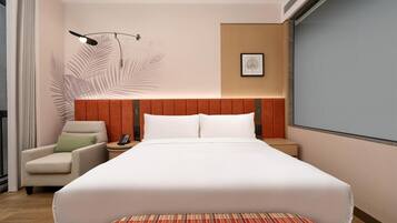 A hotel room with a large bed, a chair, a nightstand, a lamp, and a framed picture on the wall.