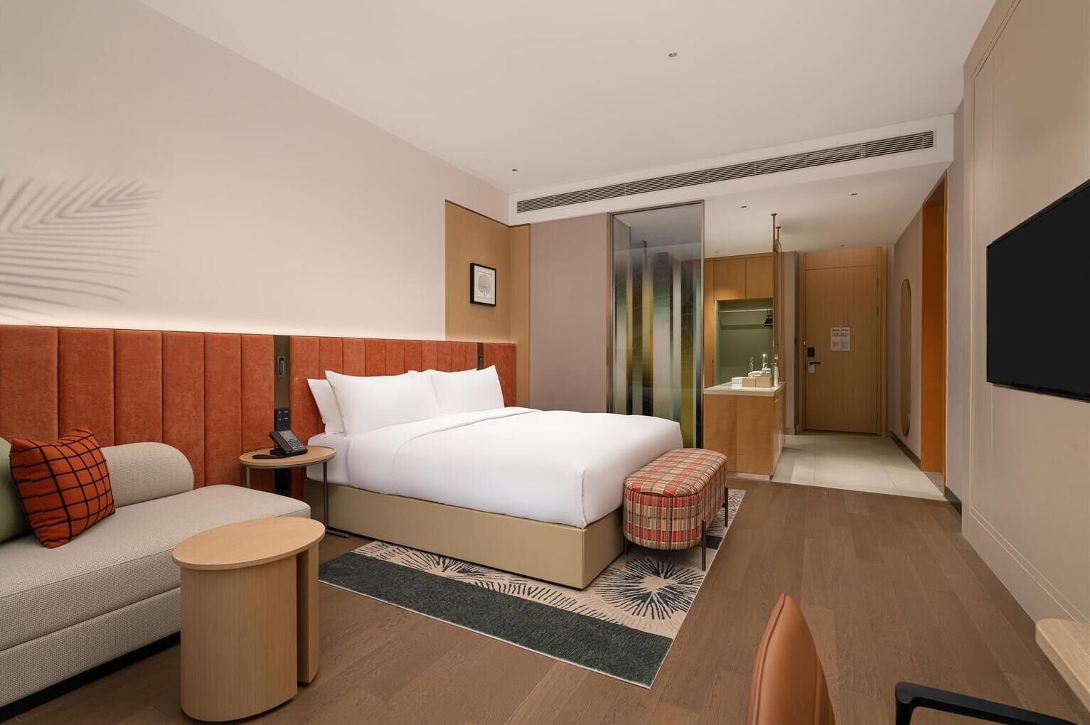 A hotel room with a bed, a sofa, a small round table, a chair, a bathroom, and a TV.