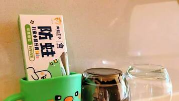 Una taza verde con cara de caricatura, una taza de vidrio transparente y una caja de fideos instantáneos sobre una encimera.