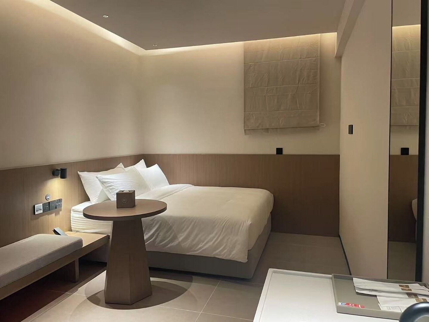 A modern hotel room with a bed, bedside table, and a small round table.
