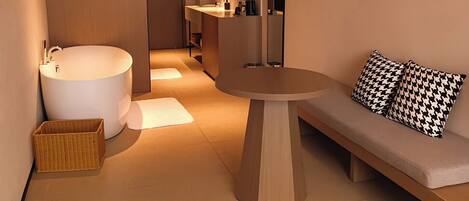 A modern bathroom with a freestanding bathtub, a round table, and a sofa with patterned cushions.