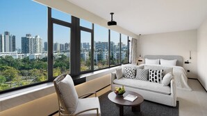 A modern hotel room with a city view, a sofa, a chair, a coffee table, and a bed with patterned pillows. - SOVIS PLUS HOTEL (Shenzhen)