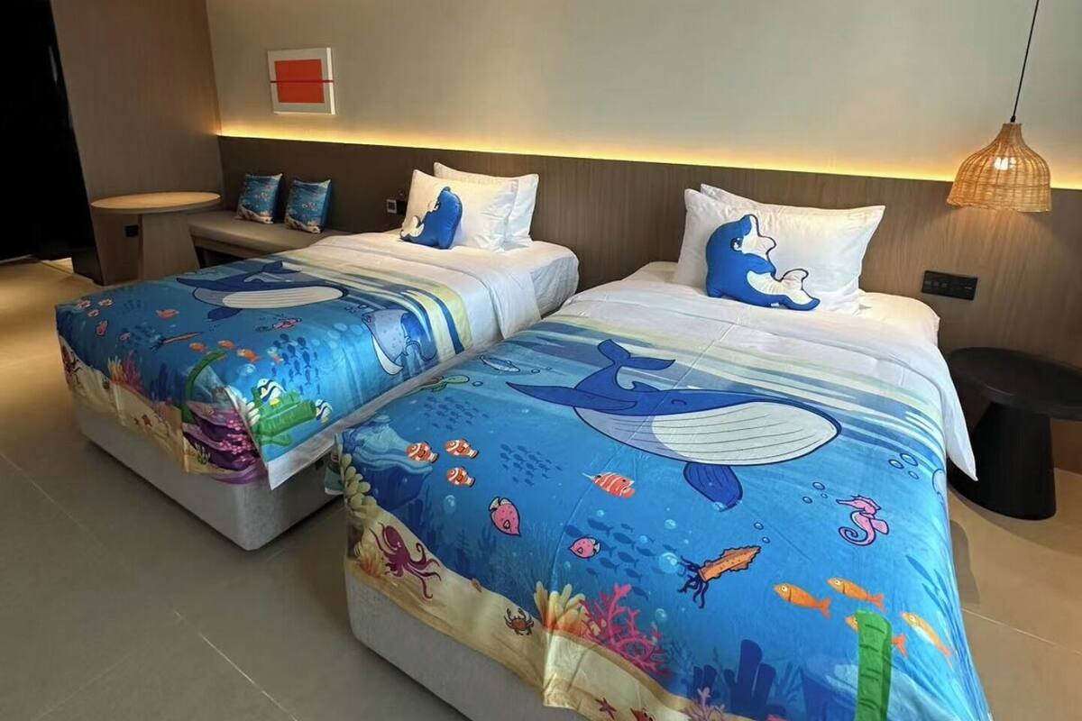 Una habitación de hotel moderna con dos camas, una mesita pequeña y un aplique de pared.