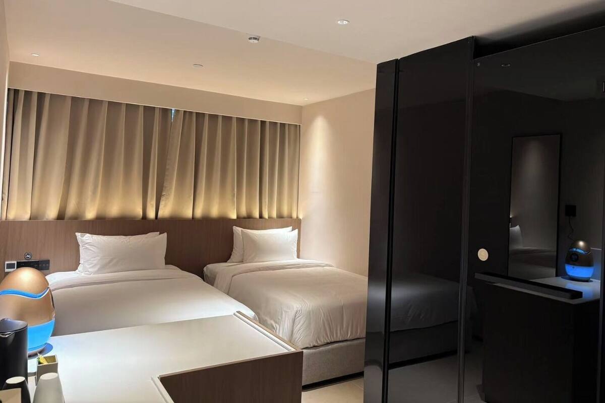 Habitación de hotel con dos camas, un escritorio con lámpara, minibar y un espejo grande.