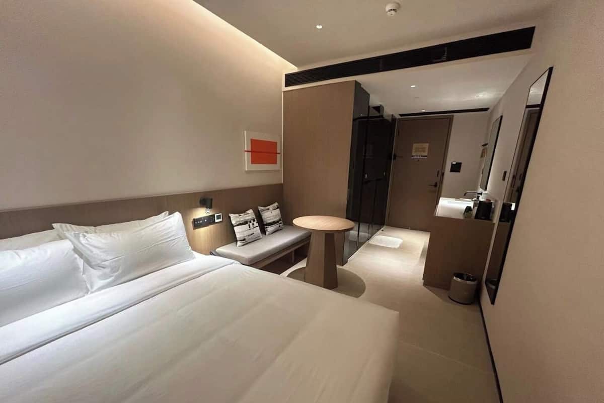 Una habitación de hotel moderna con una cama grande, mesitas de noche, una pequeña mesa redonda y un espejo.