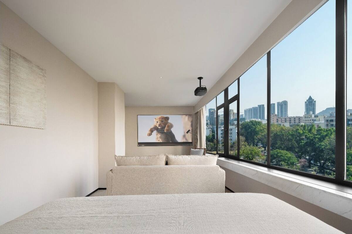 Un dormitorio con vistas a la ciudad, una ventana grande, una cama y un televisor de pared.