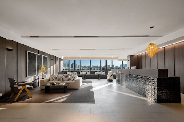 A modern living room with a sofa, coffee table, and a view of the cityscape through large windows.