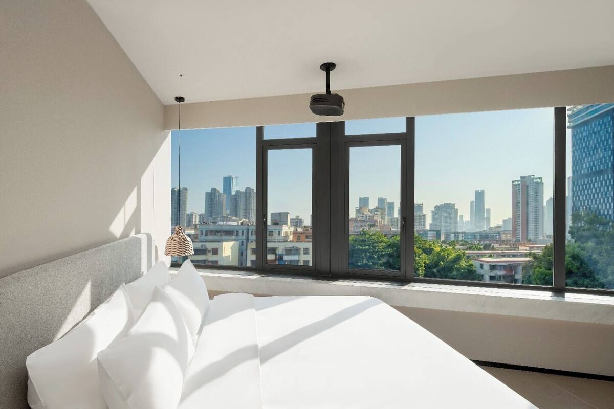 Un dormitorio con un ventanal grande, una cama y una lámpara colgante.