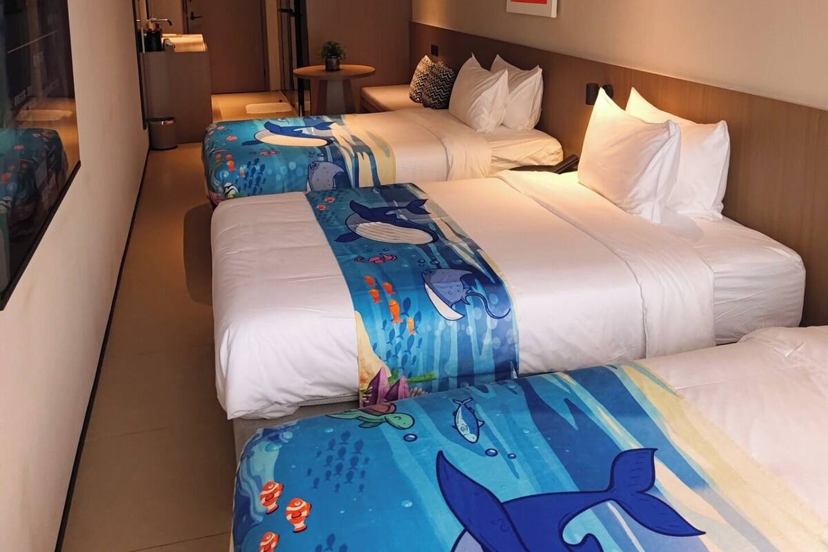 Habitación de hotel con dos camas, una mesita, una silla, una puerta y una lámpara fijada a la pared.