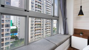A modern room with a large window, a built-in bench, a bedside table with a vase, and a hanging pendant light. - Scenic Valley Serviced Apartment (Ho Chi Minh City)