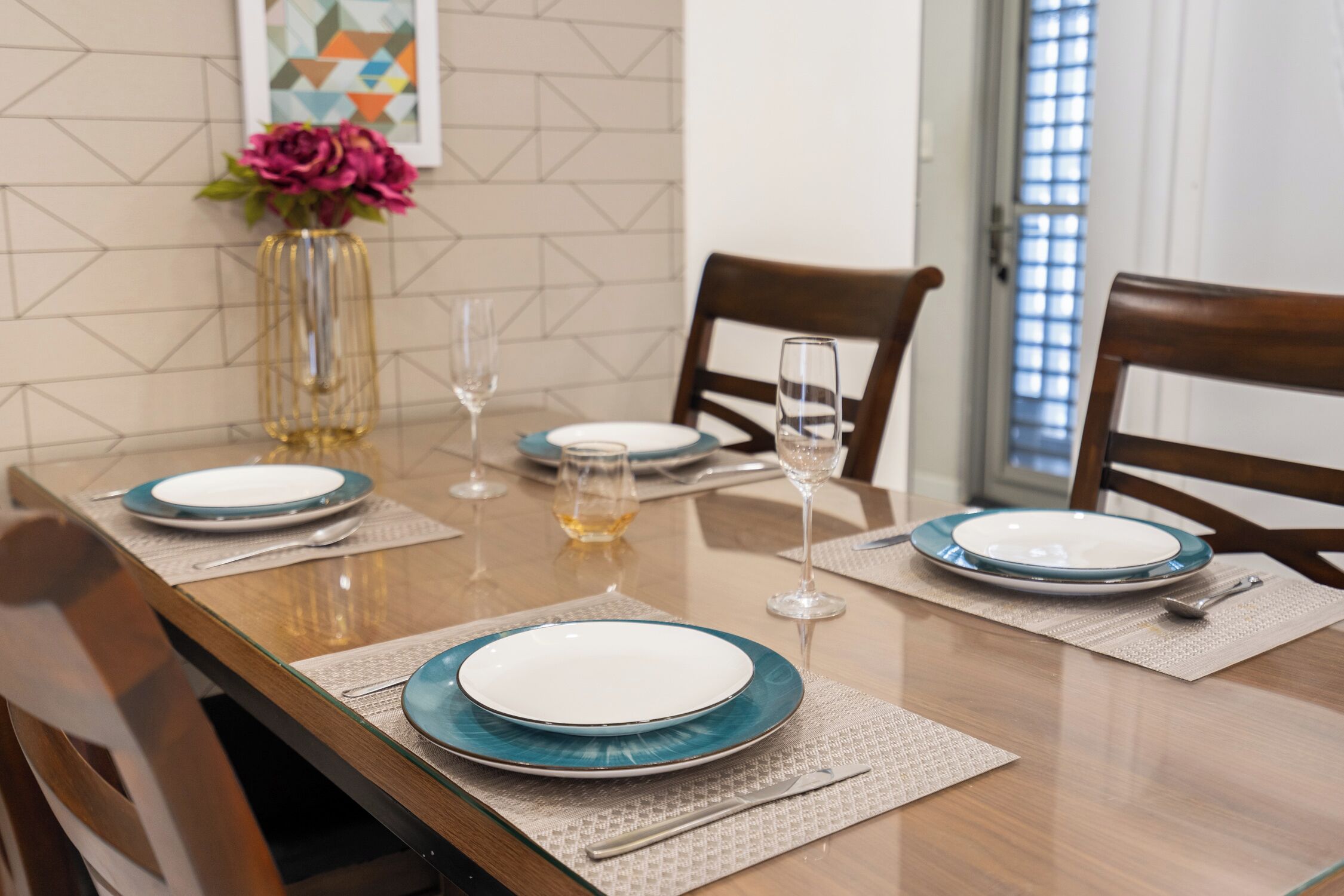 Una mesa de comedor dispuesta con platos, vasos y un jarrón con flores.