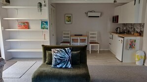 Un espace de vie compact comprenant un canapé, une table à manger, des chaises, un coin cuisine et une armoire blanche.