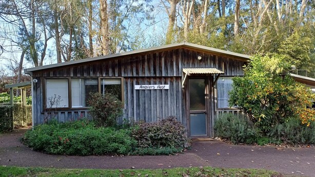 Un bâtiment rustique en bois, portant l’inscription « Amblers Rest », avec une porte, des fenêtres et un petit espace porche.