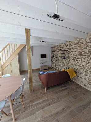 Ein Zimmer mit einer Holztreppe, einem braunen Sofa, einem Esstisch mit Stühlen und einer Steinwand.