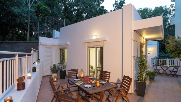 An outdoor patio with a dining table, chairs, potted plants, and a railing. - Haven Home: Central & Quiet- Elli Beach & Old Town (Rodos)