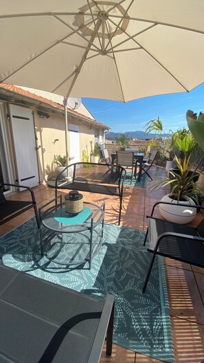 Eine Terrasse im Freien mit Tisch, Stühlen, einem großen Sonnenschirm und Topfpflanzen.