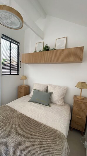 Ein Schlafzimmer mit einem Bett, Nachttischen, einem Fenster mit Jalousien und einem Wandregal mit Dekoration.