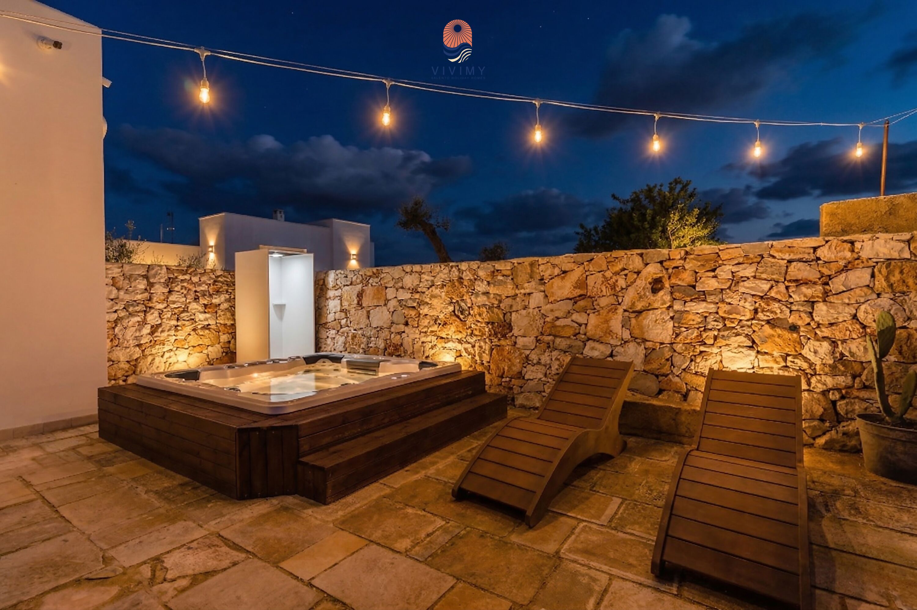 Un mur de pierres, un jacuzzi et des chaises longues en bois, le tout dans un cadre extérieur.