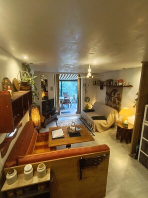 A cozy living room with a sofa, a coffee table, and a bookshelf. There is a dining area with a table and chairs visible through the doorway.
