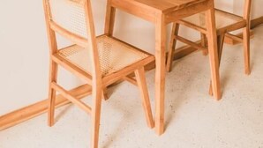 Una mesa de madera con dos sillas de mimbre, una botella de vidrio y un vaso sobre la mesa.
