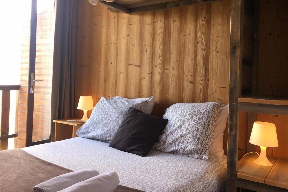 Habitación con paneles de madera, una cama, dos lámparas de noche y un ventanal.