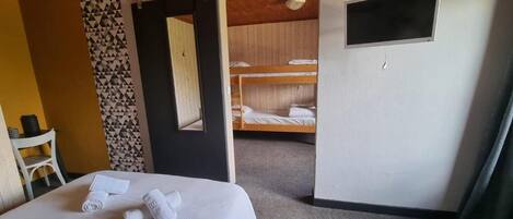 A hotel room with a bed, a desk, a chair, a door leading to a bunk area, and a small TV.