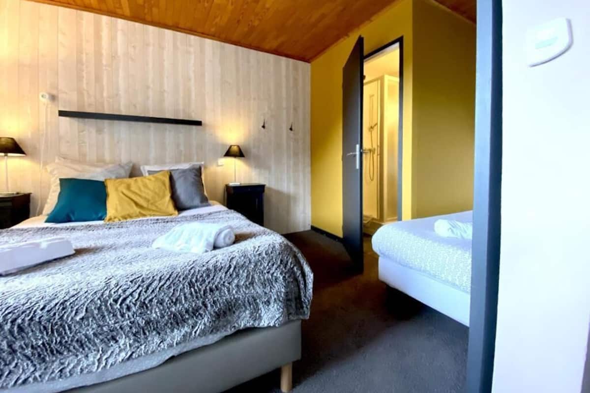 Un dormitorio con cama, mesita de noche, lámpara y una puerta que da al baño.