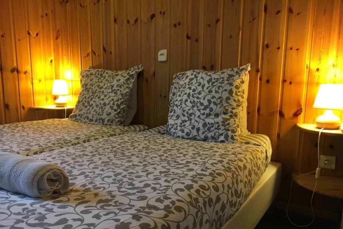 Cama doble con ropa de cama estampada, dos lámparas de noche y una toalla enrollada sobre la cama.