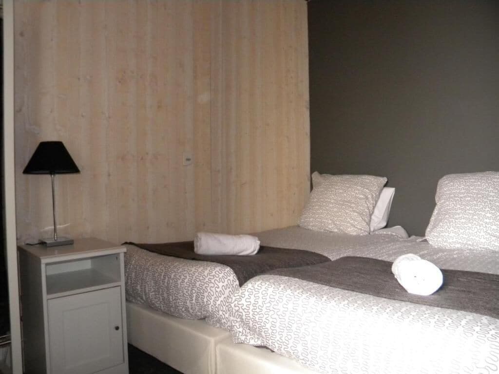 A bedroom with two beds, a bedside table, and a lamp.
