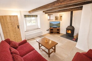 A cozy living room with a fireplace, a television, and a red sofa. - Claybottom Farm, Caldbeck - in a rural setting with fell walks from the door (Hesket Newmarket)