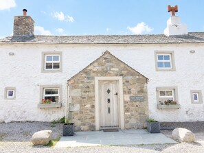 A stone building with a white facade, a central door, and a chimney. - Claybottom Farm, Caldbeck - in a rural setting with fell walks from the door (Hesket Newmarket)