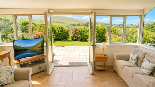 Una sala de estar con televisión, sofá, mesita de madera y puerta que da a un jardín.