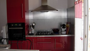 Una cocina compacta con gabinetes rojos, una estufa a gas, horno integrado y cafetera.