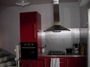A kitchen with a red cabinet, stainless steel range hood, and a gas stove. - Chickadee House (Saint-Palais-sur-Mer)