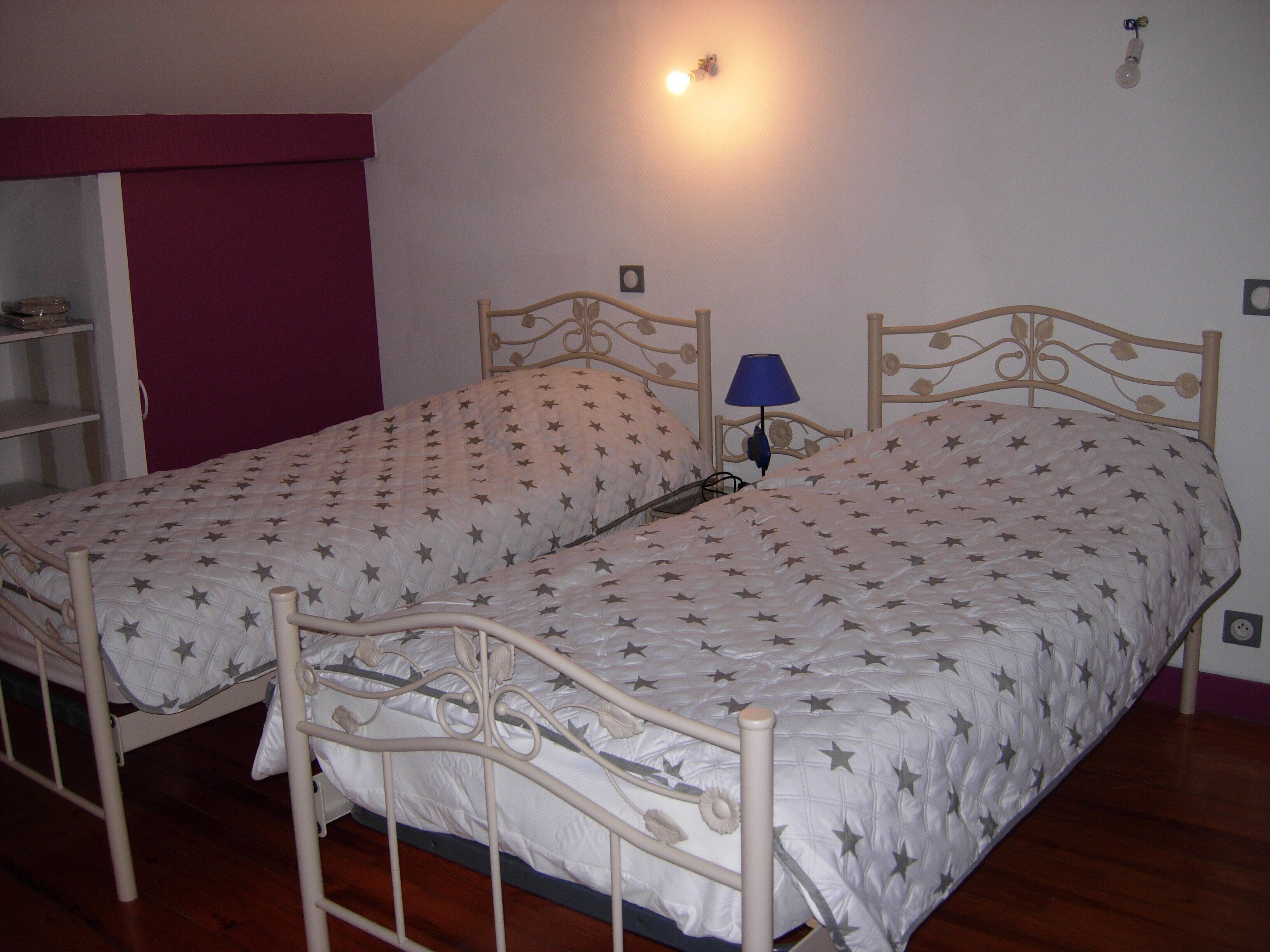 A twin bed with a star-patterned bedspread, a bedside table with a lamp, and a wooden floor.