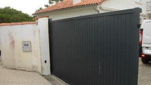 Una reja de metal negro con un muro blanco y un techo de tejas rojas al fondo.