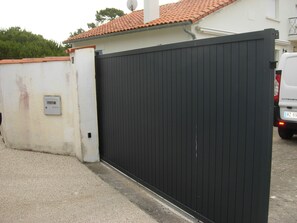 A gated area with a white wall, a black gate, and a vehicle parked nearby. - Chickadee House (Saint-Palais-sur-Mer)