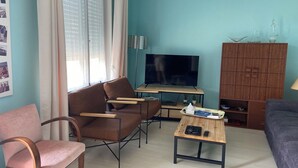 Una sala de estar con un sofá, dos sillones, una mesa de centro, un televisor y un mueble de madera.