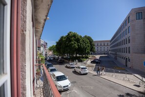 Straßenansicht mit parkenden Autos, einer von Bäumen gesäumten Straße und einem Gebäude mit moderner Fassade.