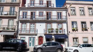 Un edificio de varios pisos con balcones, una fachada comercial y coches estacionados.