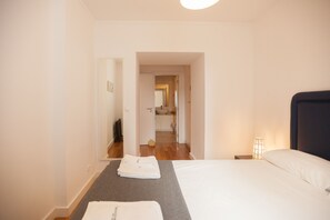Ein Hotelzimmer mit Bett, Nachttisch, Lampe, Handtuch und Blick auf ein Badezimmer und eine Küche durch eine offene Tür.