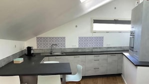 Eine moderne Küche mit dunkler Arbeitsplatte, weißen Stühlen und einem Fliesenspiegel mit Muster.