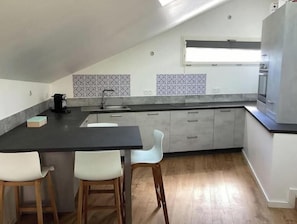 A modern kitchen with a dark countertop, white chairs, and patterned backsplash tiles. - Quiet location between lake and mountains - Apartment with garden near Annecy (Sevrier)