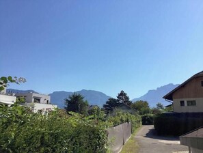 A residential area with houses, a narrow road, and mountains in the background. - Quiet location between lake and mountains - Apartment with garden near Annecy (Sevrier)
