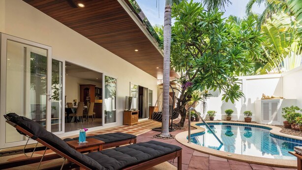 Ein moderner Poolbereich im Freien mit Liegestühlen, einem Essbereich und einem großen Baum.