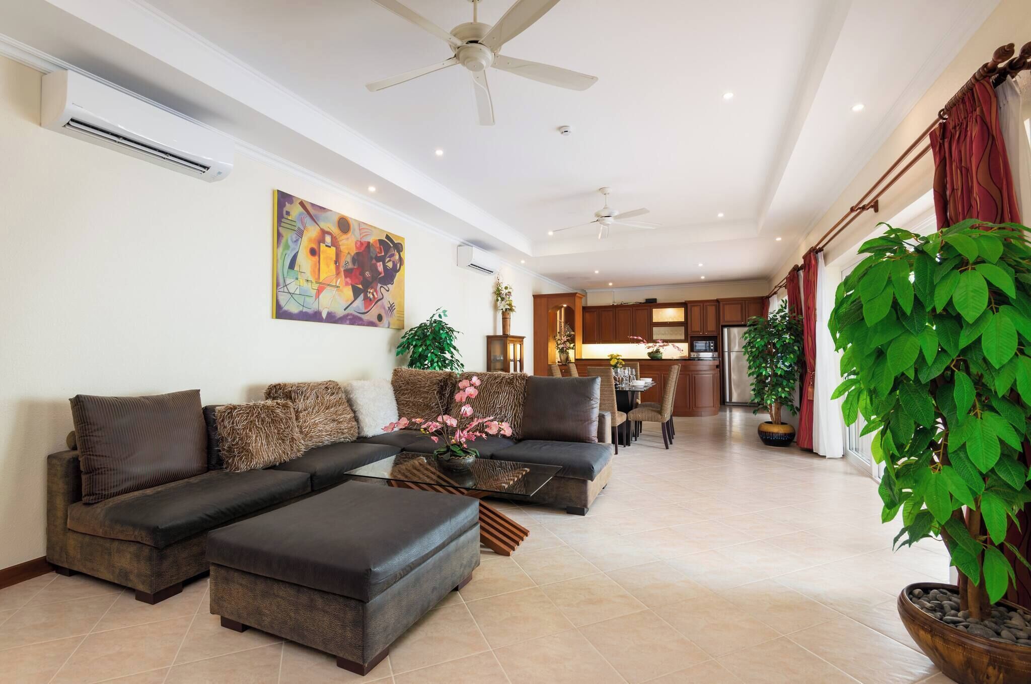 Una sala de estar con sofá modular, reposapiés, ventiladores de techo y una planta grande en maceta.