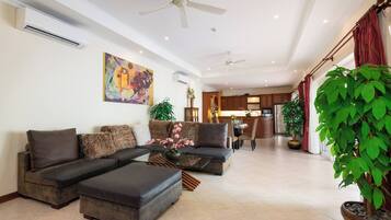 A living room with a sectional sofa, ottoman, ceiling fans, and a large potted plant.