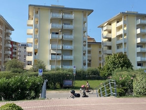 Ein mehrstöckiges Wohngebäude mit Balkonen, eine gepflasterte Fläche mit einem Rollroller und einem Fahrrad, sowie ein Schild, das einen Parkplatz kennzeichnet.