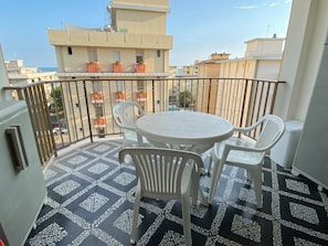 Ein Balkon mit rundem Tisch und zwei Stühlen, einem gemusterten Boden und Blick auf Gebäude im Hintergrund.