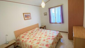 Ein Schlafzimmer mit Bett, Schreibtisch, einem Fenster mit Vorhängen und einem Wandbild.